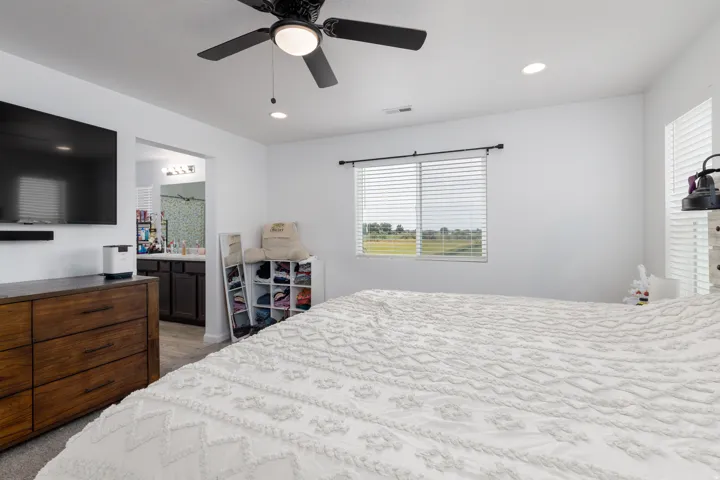 Recessed lighting, ceiling fan, window with horizontal blinds, and an attached full bathroom featuring a dual vanity with dark wood-finish cabinetry