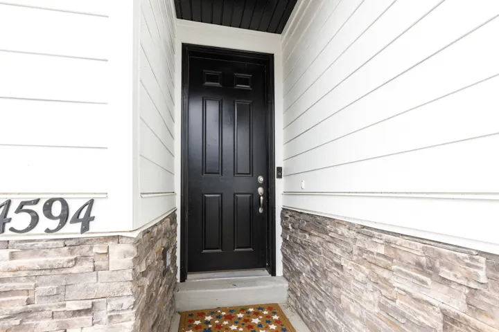 Black paneled entry door with polished hardware, complemented by white horizontal siding and a stacked stone facade