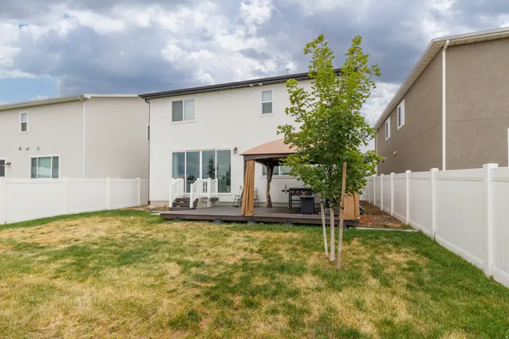 Expansive backyard featuring a white vinyl fence, spacious wood-finish deck, and sliding glass doors