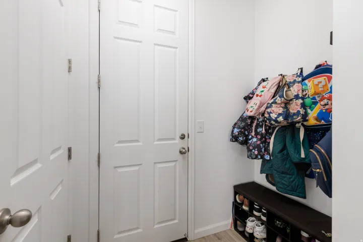 White six-panel interior door, light wood-finish flooring, white walls, and a built-in storage bench with shoe compartments
