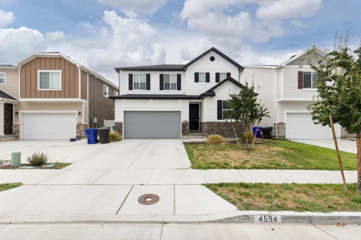 Modern exterior with white siding, black window shutters, a stone accent facade, an attached garage, and a concrete driveway