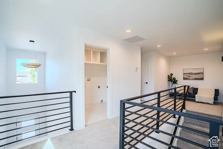 Open hallway with modern horizontal metal railings, recessed lighting, and a laundry closet with built-in shelving