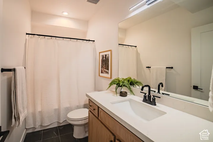 Bathroom featuring a wood-finish vanity with a white countertop and integrated sink, black hardware, a shower with a white curtain, and dark tile flooring