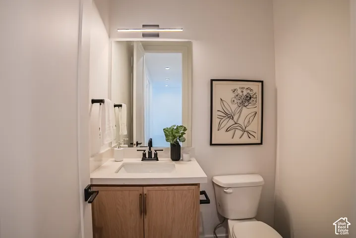Modern vanity with a light wood-finish cabinet, white countertop, rectangular undermount sink, and black faucet