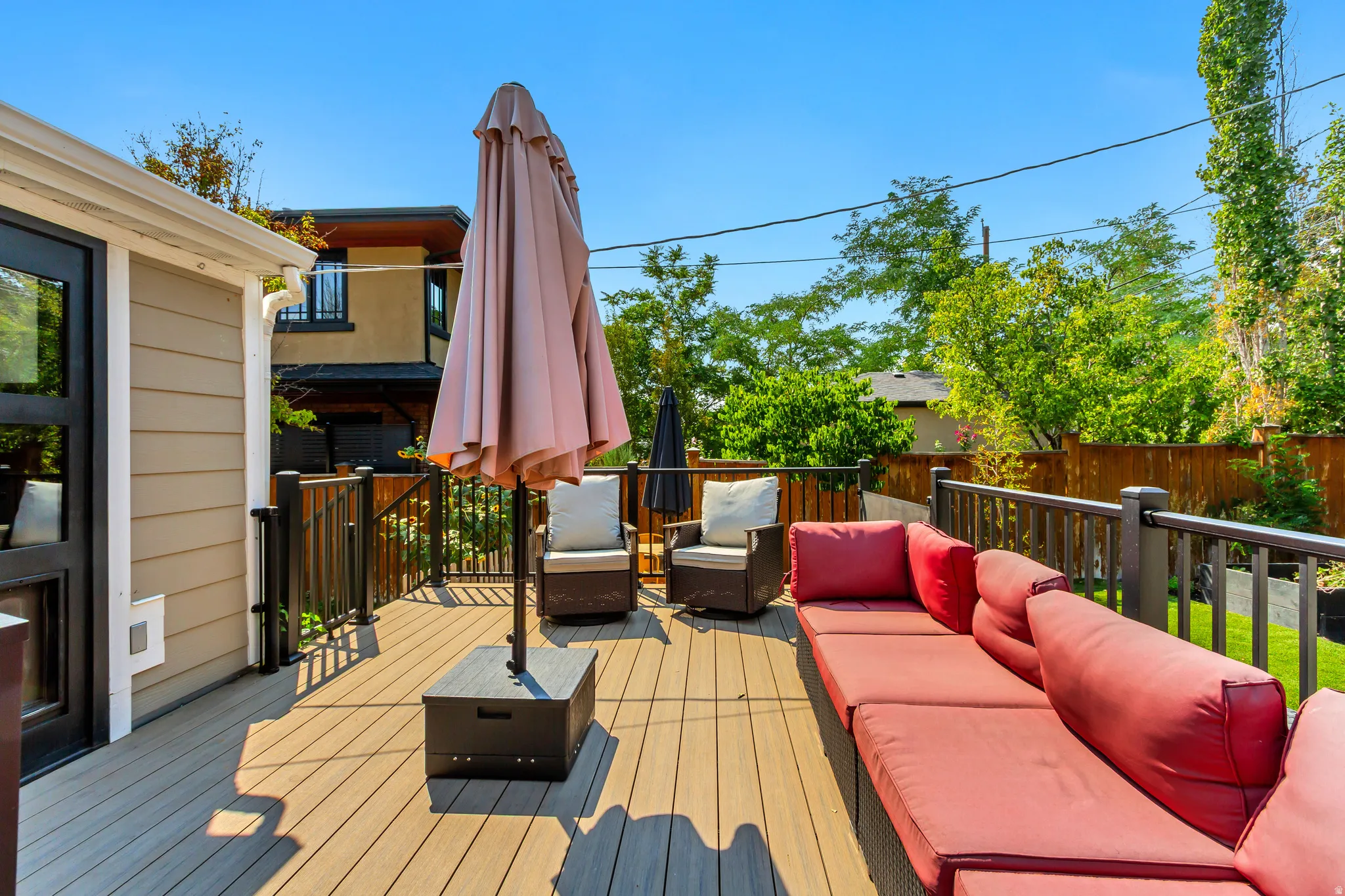 Expansive composite deck featuring dark railings, a wood-paneled exterior, and a glass-paneled door