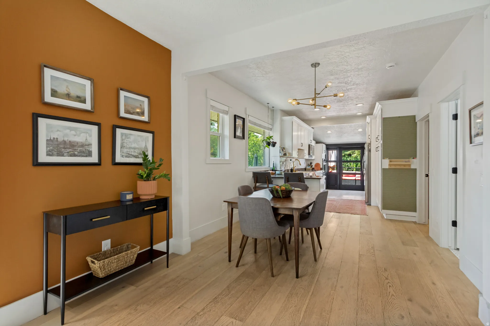 Open-concept dining area featuring light wood-finish flooring, a contemporary linear chandelier, and a bright kitchen beyond