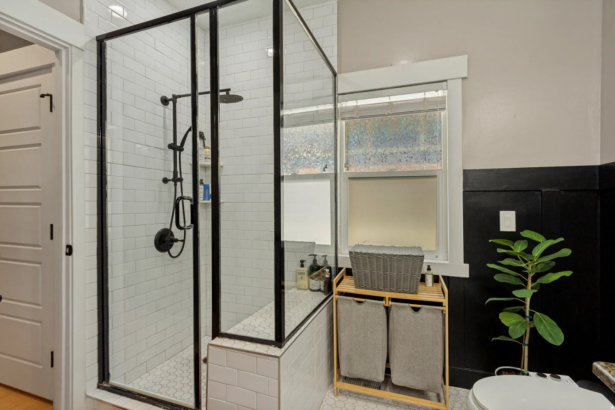 Glass-enclosed shower with matte black fixtures, white subway tile walls, a built-in shower bench, and a hexagonal tile floor