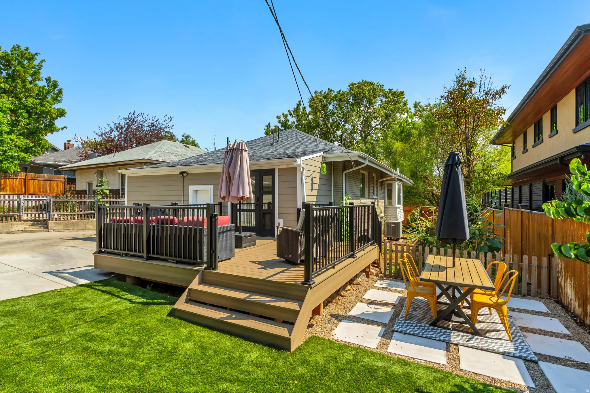 Expansive backyard featuring a composite deck with dark railings, a manicured lawn, and a stone paver patio