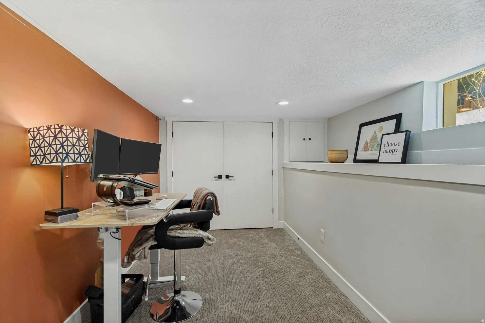 Recessed ceiling lighting, textured carpet flooring, interior partition wall, white painted doors with dark hardware, and a high-set window
