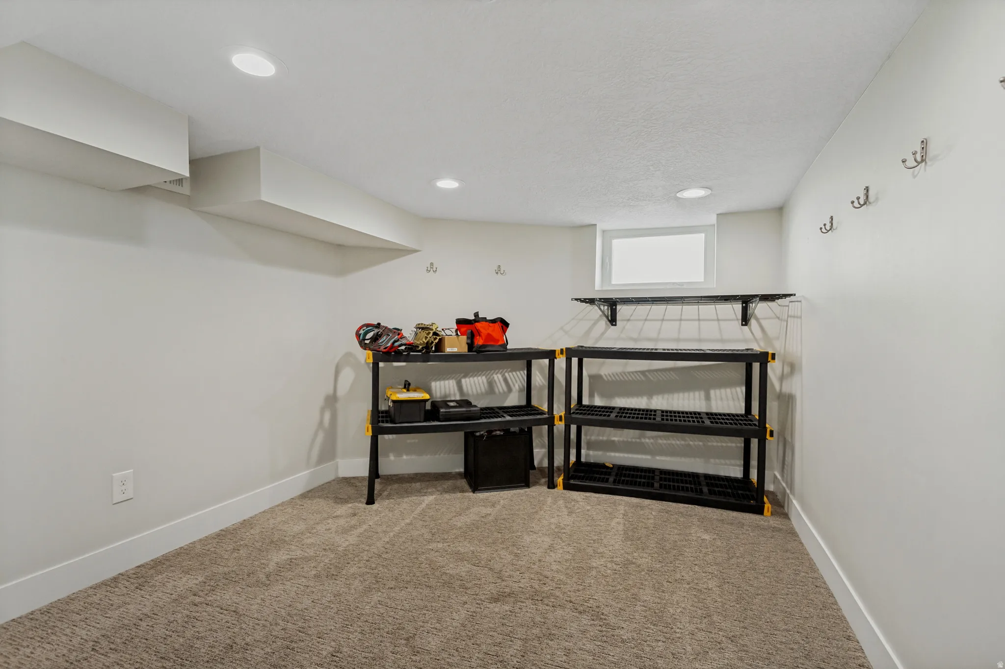 Recessed ceiling lighting, wall-mounted hooks, shelving, window, and carpet flooring