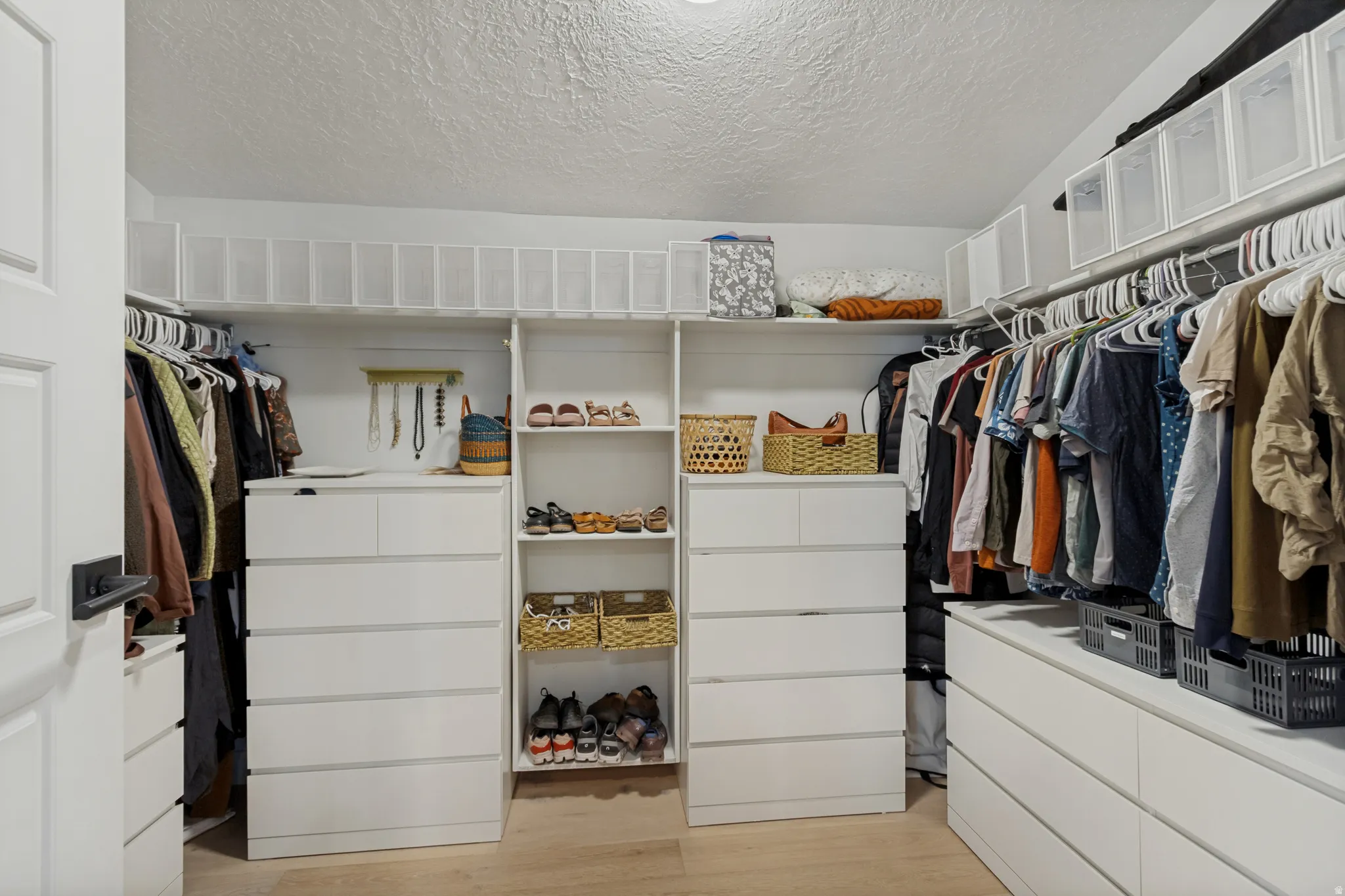 Built-in closet system featuring multiple hanging rods, white drawer units, and open shelving