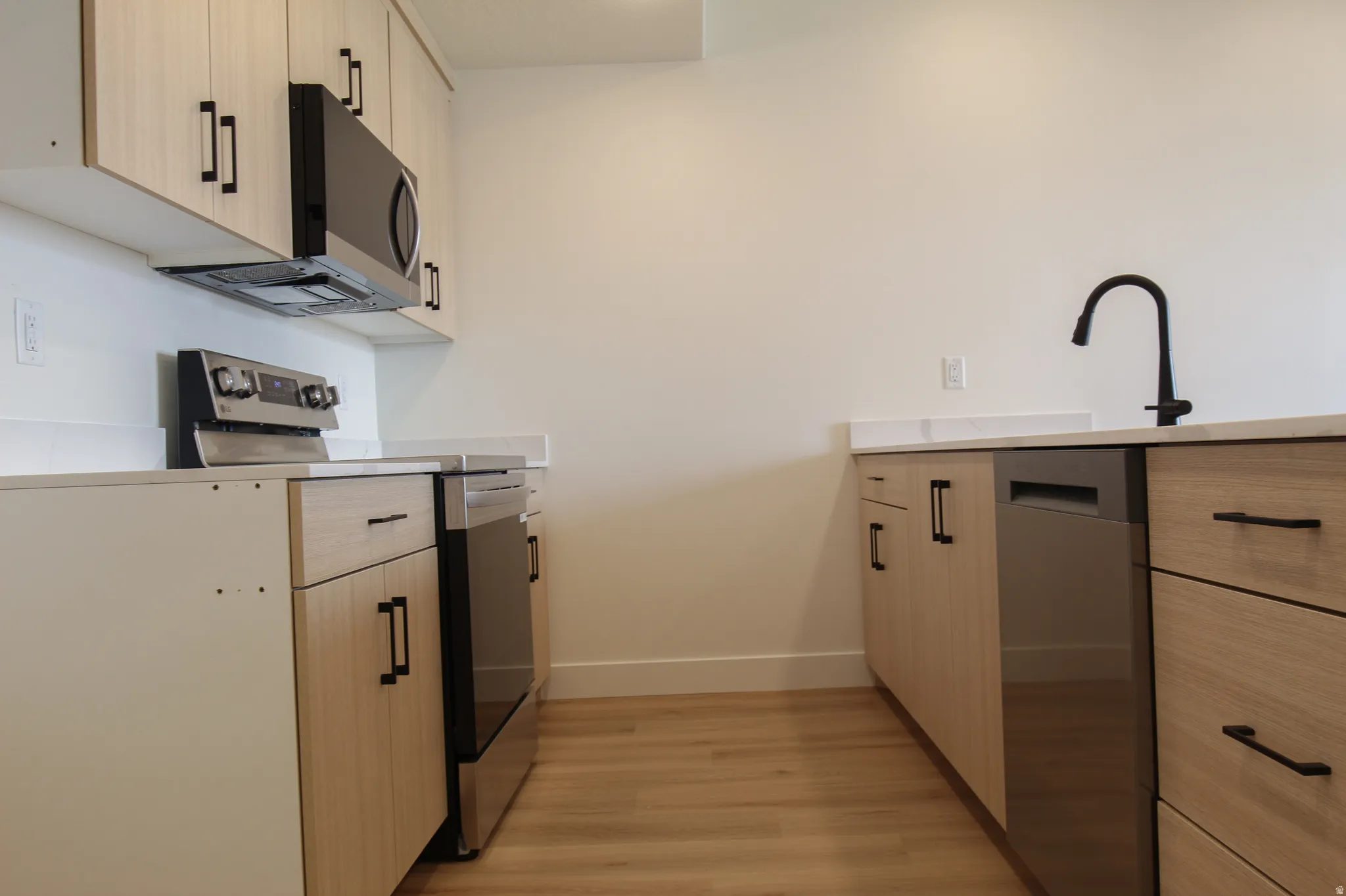 Wood-finish flooring, light-toned cabinetry with black hardware, stainless steel appliances, and a matte black gooseneck faucet