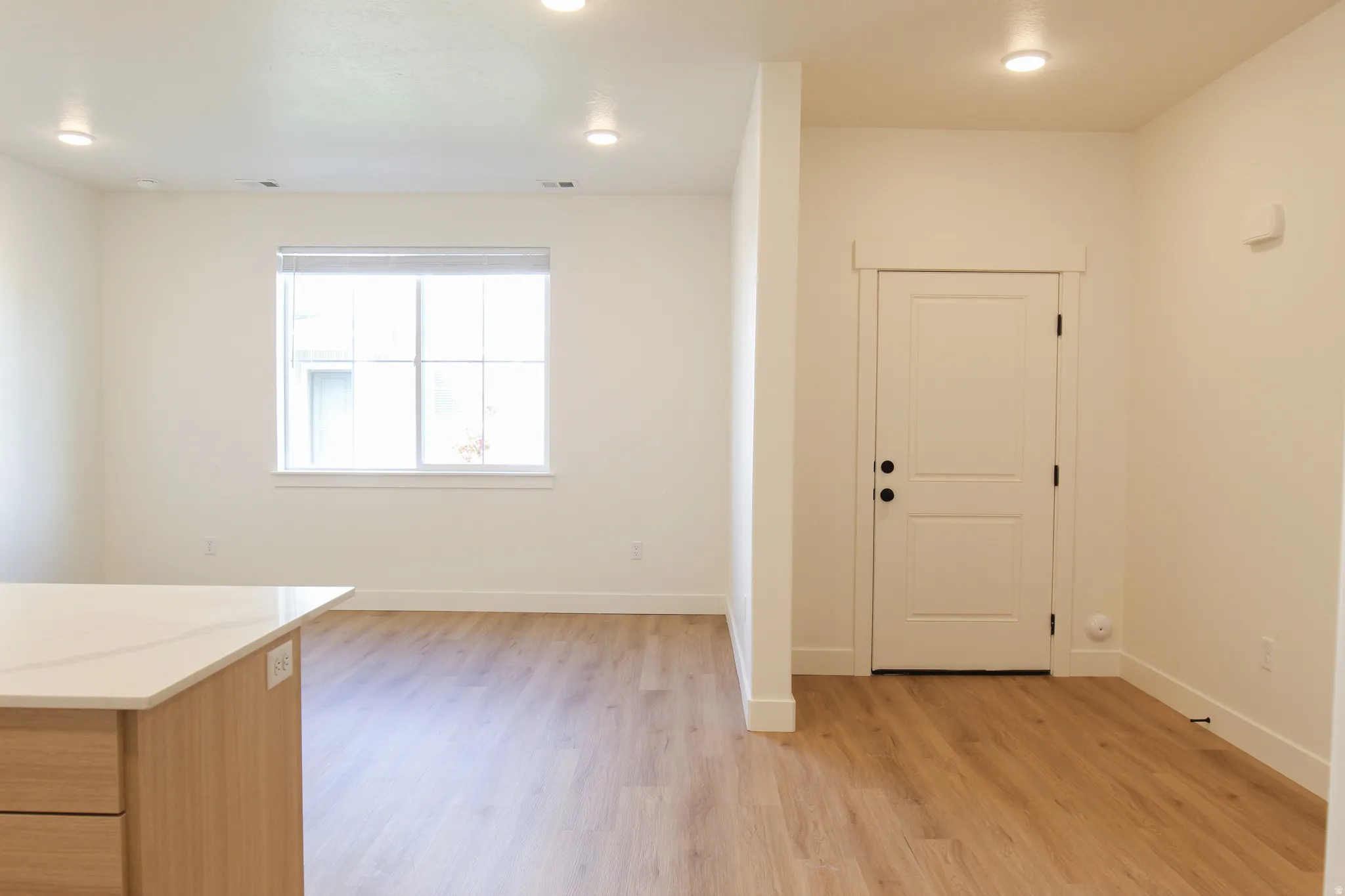 Recessed lighting, wood-finish flooring, white walls, white window trim, and a white interior door