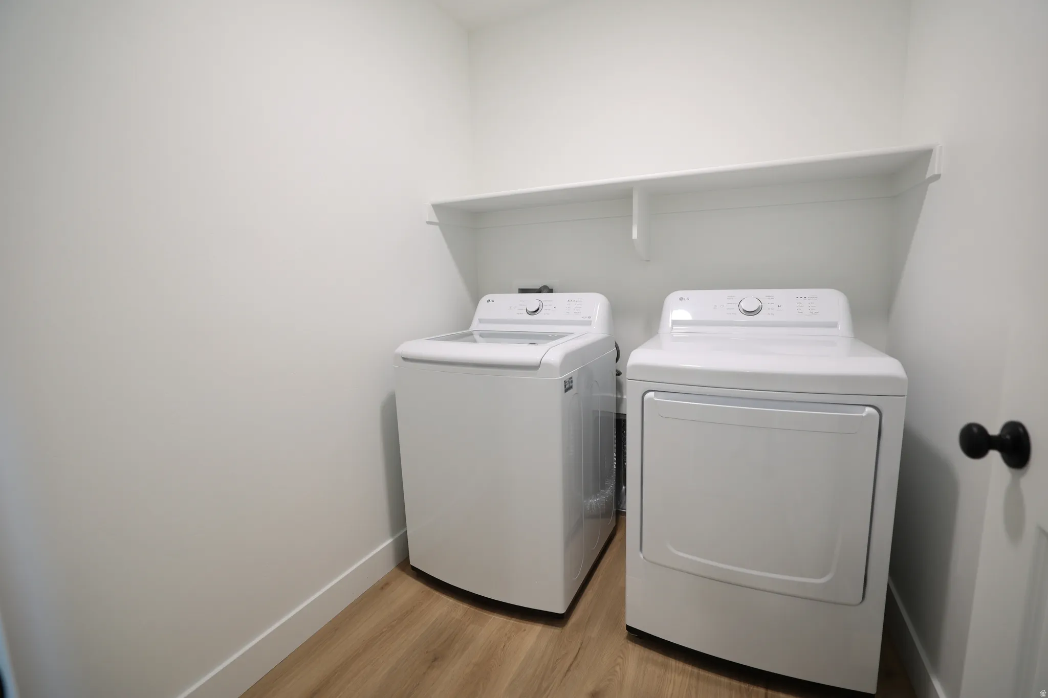 Dedicated laundry area featuring a white storage shelf, light-toned wood-finish flooring, and white walls