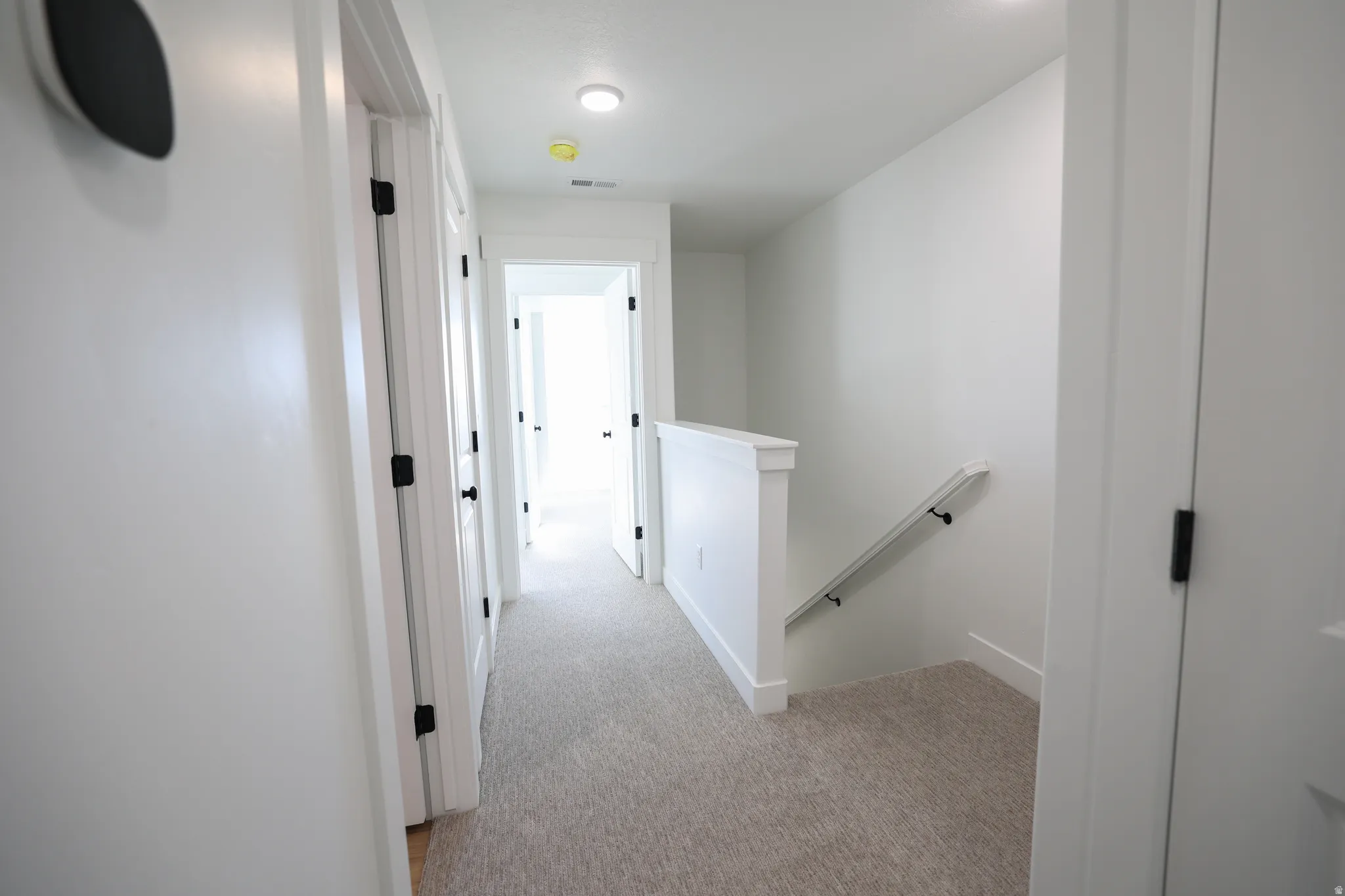 Carpeted hallway with white walls, multiple doorways with matte black hardware, and a white railing with a black handrail