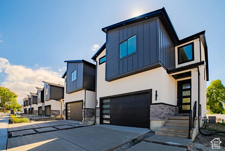 Contemporary exterior with crisp white stucco, dark vertical siding, stone accents, a modern garage door, and a sleek front entry door with obscure glass panels