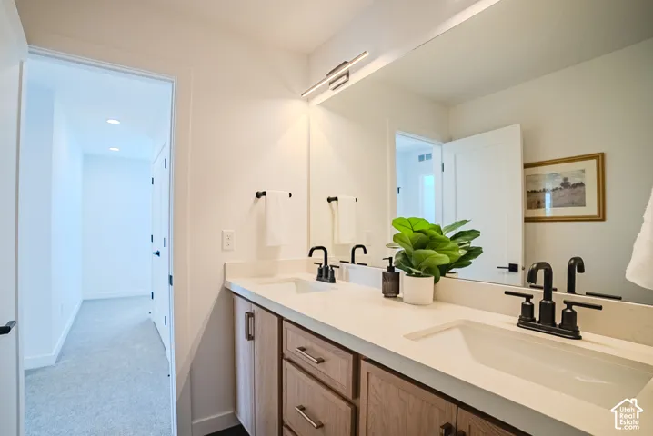 Dual sink vanity with light wood-finish cabinetry, integrated sinks, and matte black plumbing fixtures