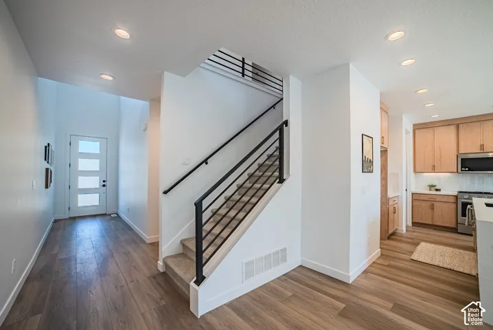 Wood-finish flooring throughout, modern staircase with black metal railings, recessed lighting, and a kitchen featuring light wood cabinetry