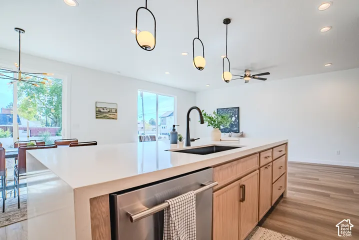 Kitchen island featuring a waterfall-edge countertop, undermount sink with a matte black faucet, integrated dishwasher, and wood-finish cabinetry
