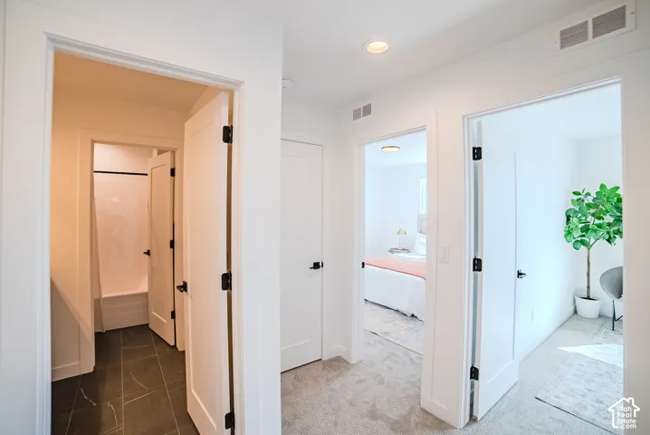 Recessed ceiling lighting, white interior doors with matte black hardware, light-toned carpeting, and dark-toned floor tiling