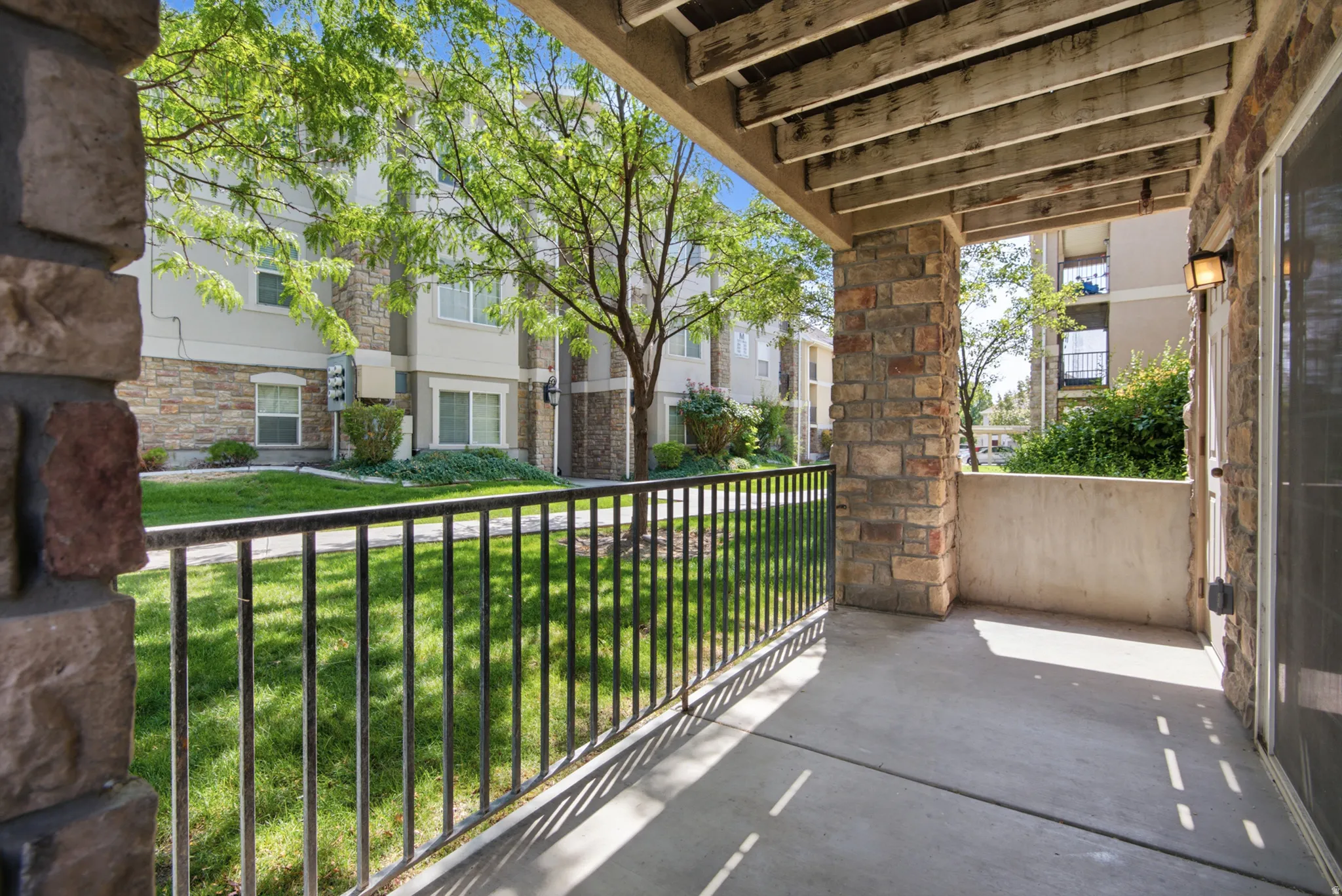 Private patio with stone columns, concrete flooring, and wrought iron railing
