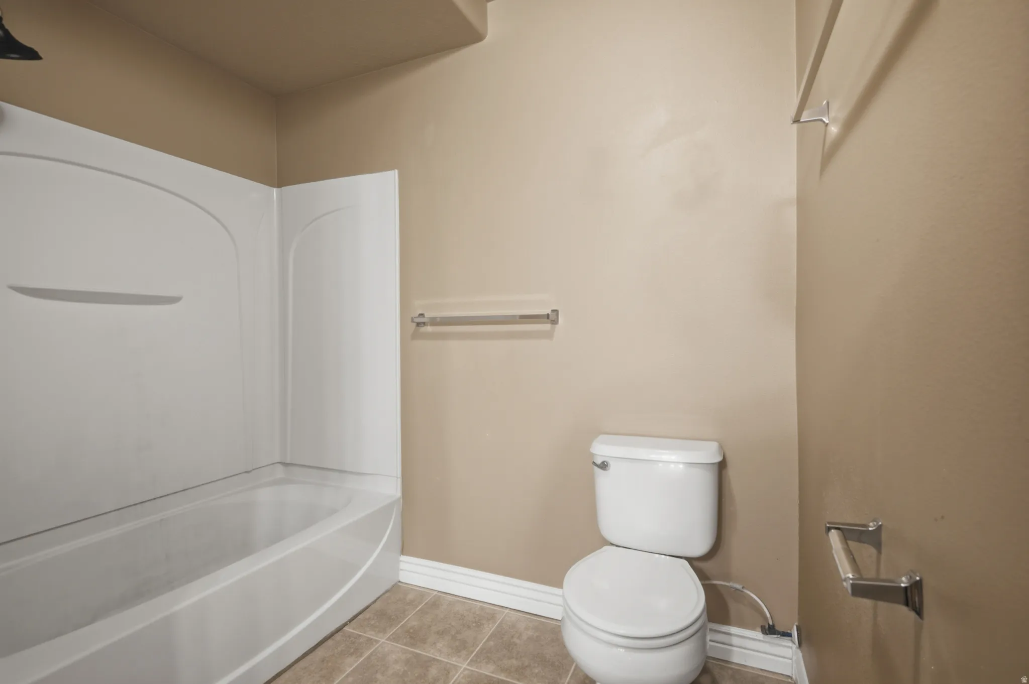 Tub-shower combination with white surround, white toilet, and tile flooring