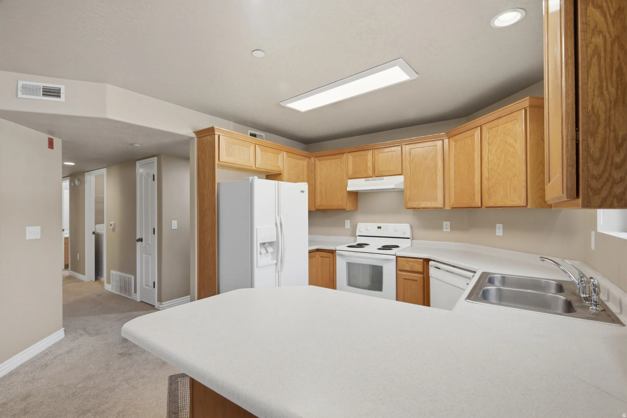 Kitchen featuring wood cabinetry, white appliances, a double basin stainless steel sink, and light-toned countertops