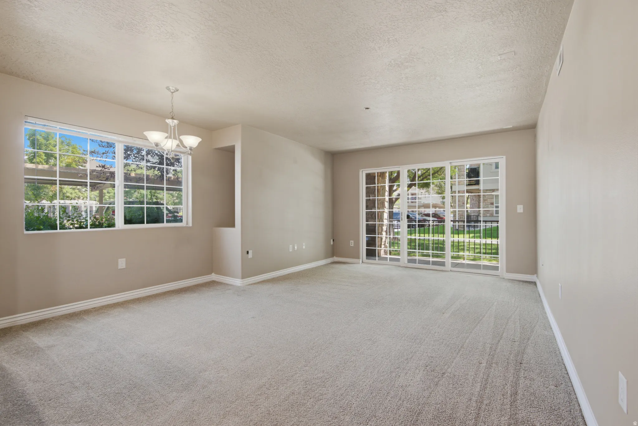Spacious room featuring neutral carpeting, a large window with grid panes, a built-in niche, and sliding glass doors