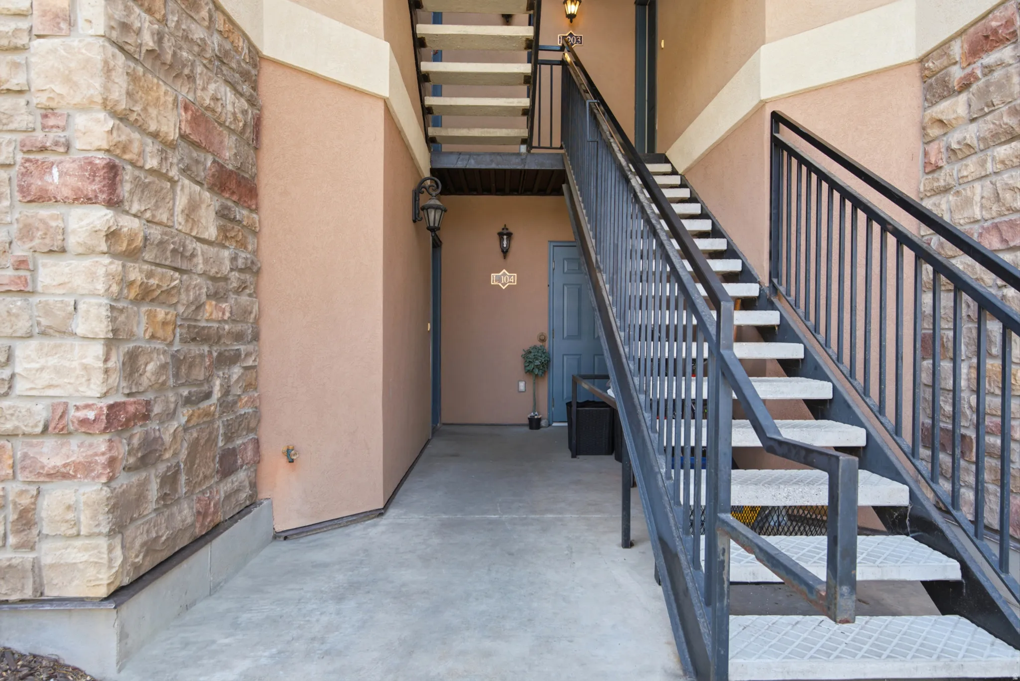 Stone veneer exterior accent, stucco siding, concrete walkway, and metal staircase with handrails