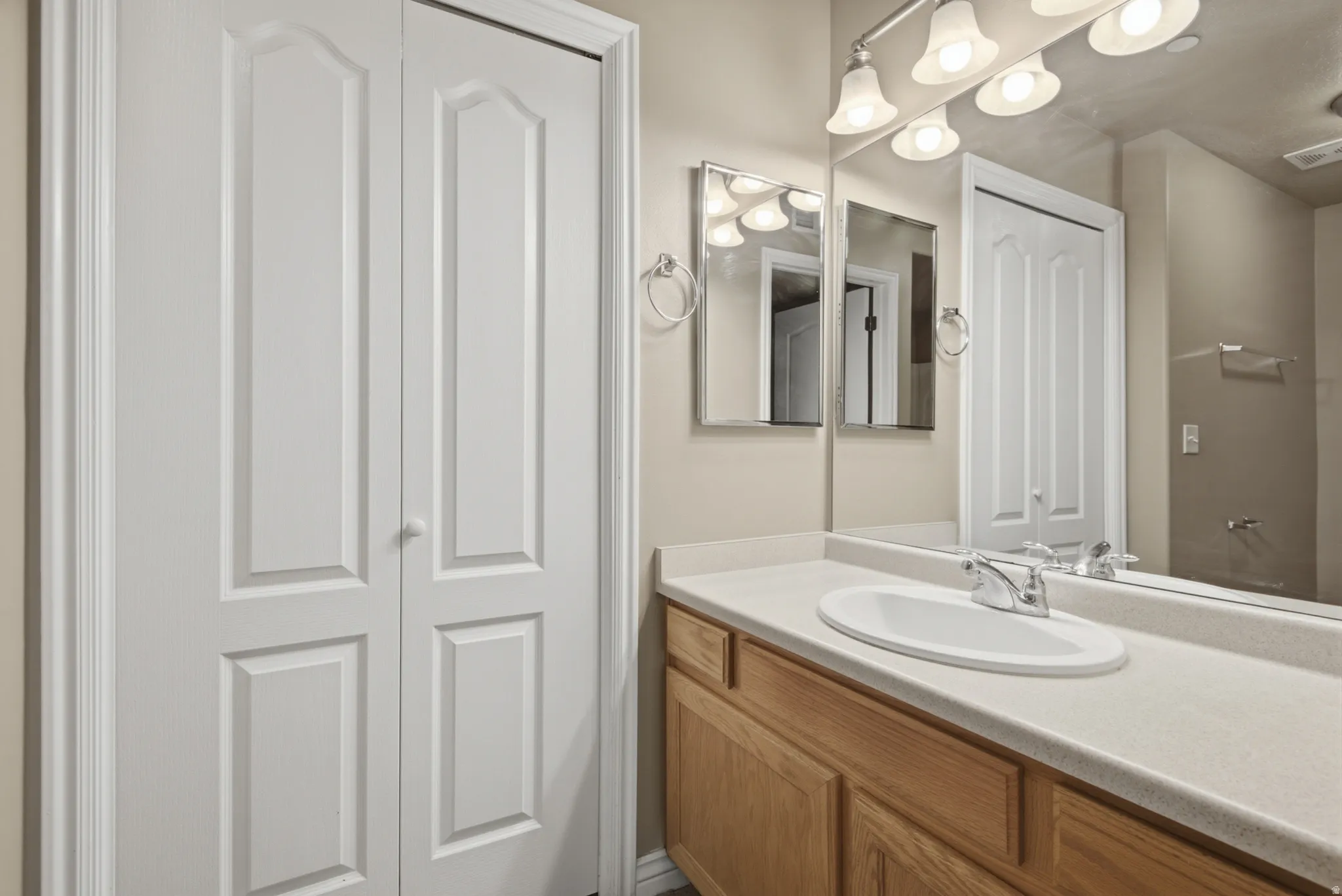 Wood-finish vanity with an integrated sink, polished chrome faucet, and expansive wall mirror