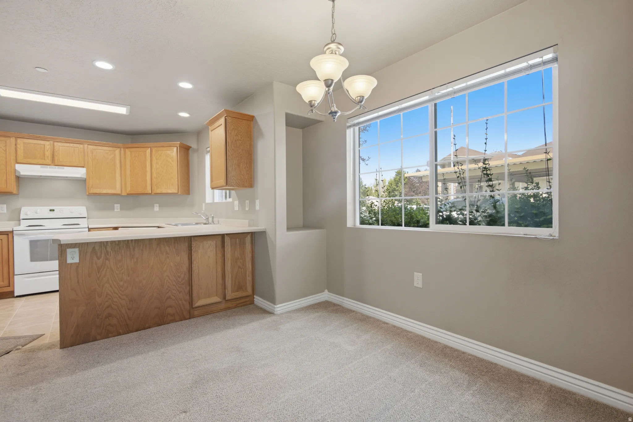 Kitchen area featuring light wood cabinetry, a white electric range, and light-toned countertops