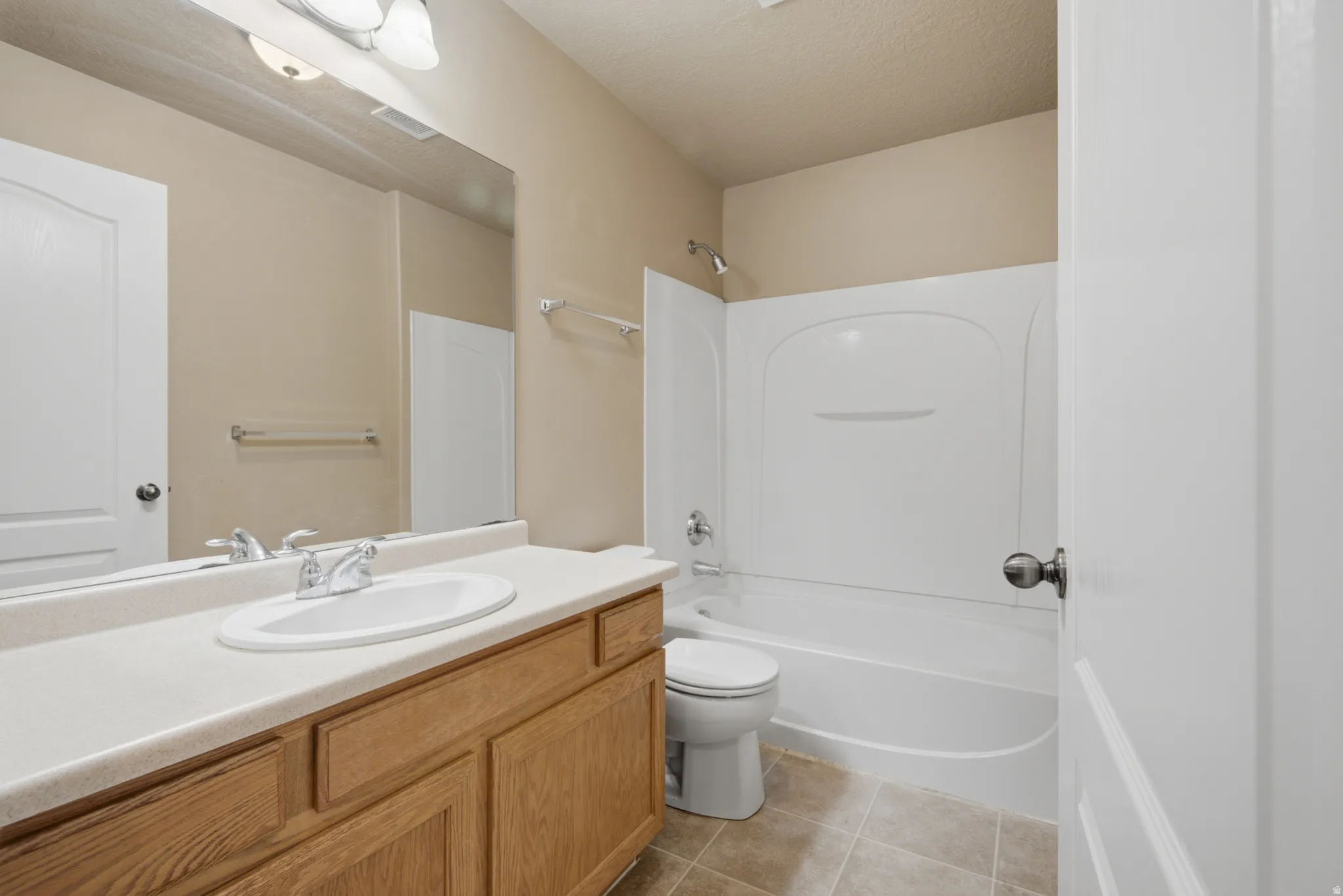 Bathroom featuring a wood-finish vanity with an integrated sink, a large wall mirror, and a white tub with shower