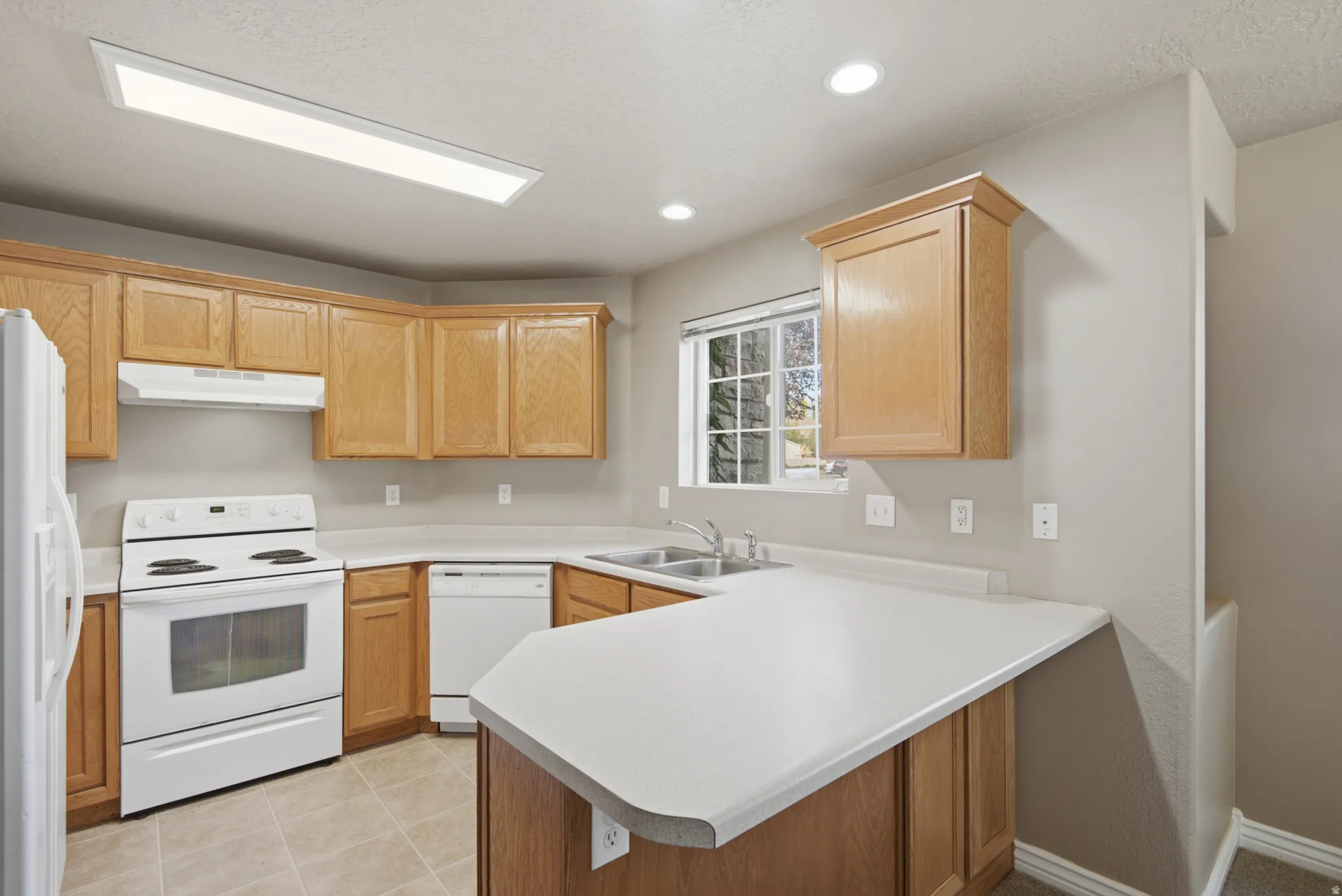 Kitchen featuring wood-finish cabinetry, white appliances, light countertops, and tile flooring