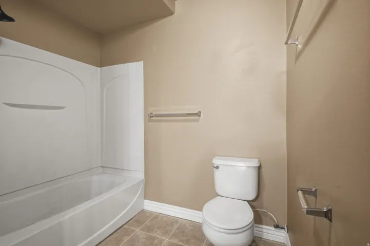Tub-shower combination with white surround, white toilet, and tile flooring