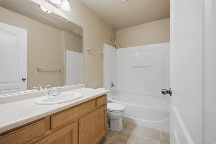 Bathroom featuring a wood-finish vanity with an integrated sink, a large wall mirror, and a white tub with shower