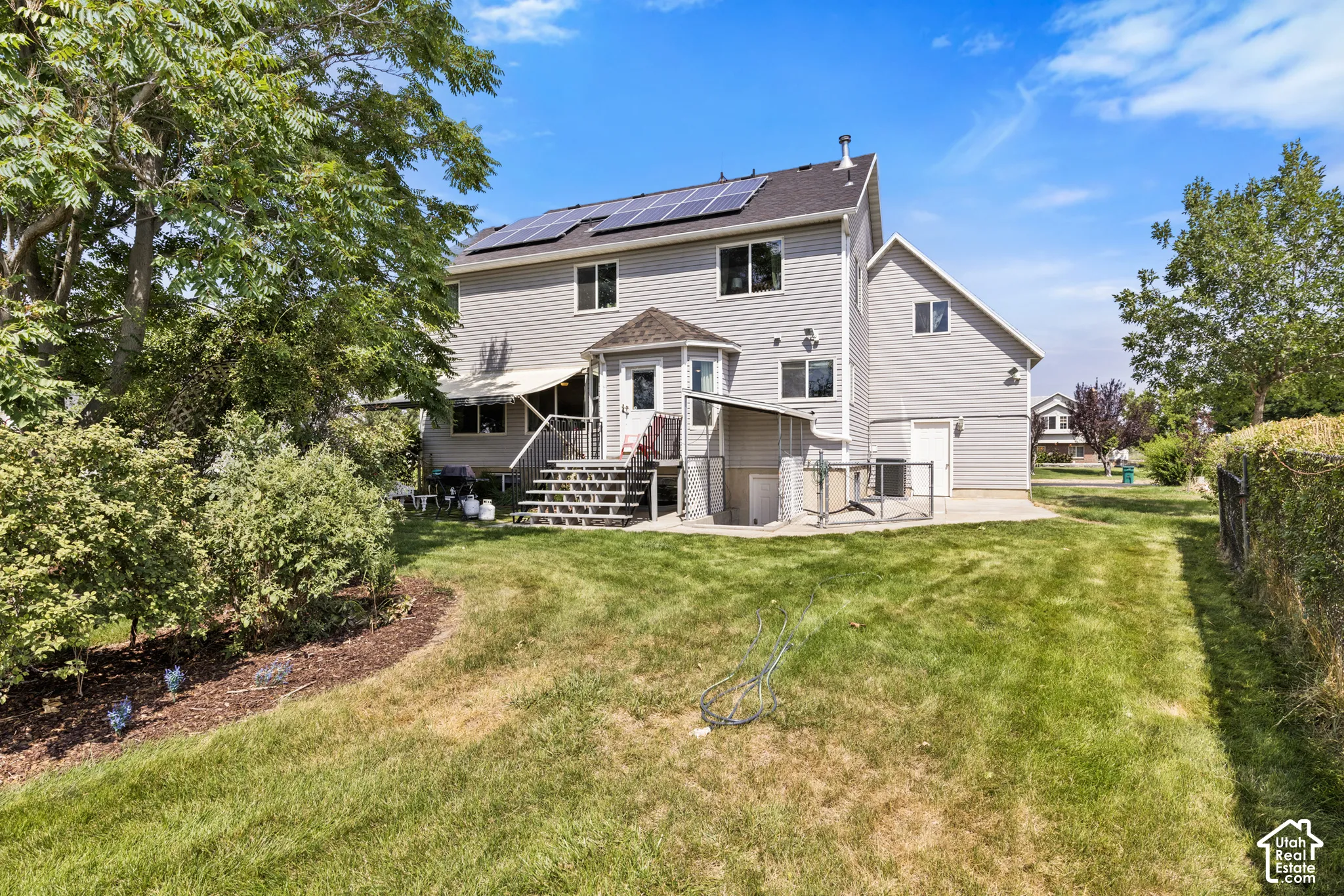 Rear exterior with solar panels, multi-level decking, an awning, and a grass lawn