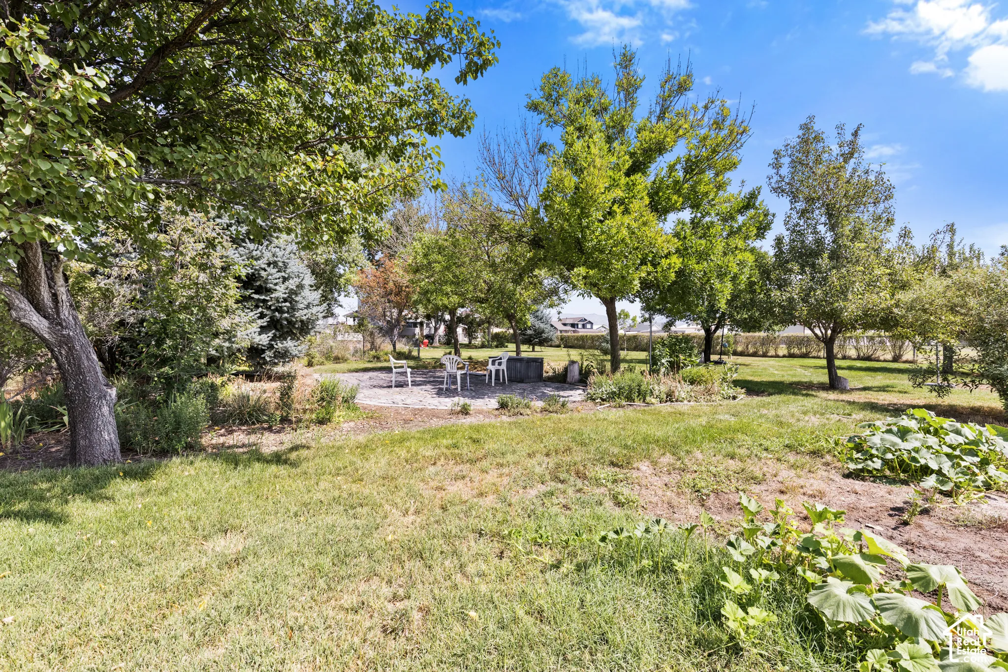 Expansive yard with mature trees, a stone patio, and established garden beds