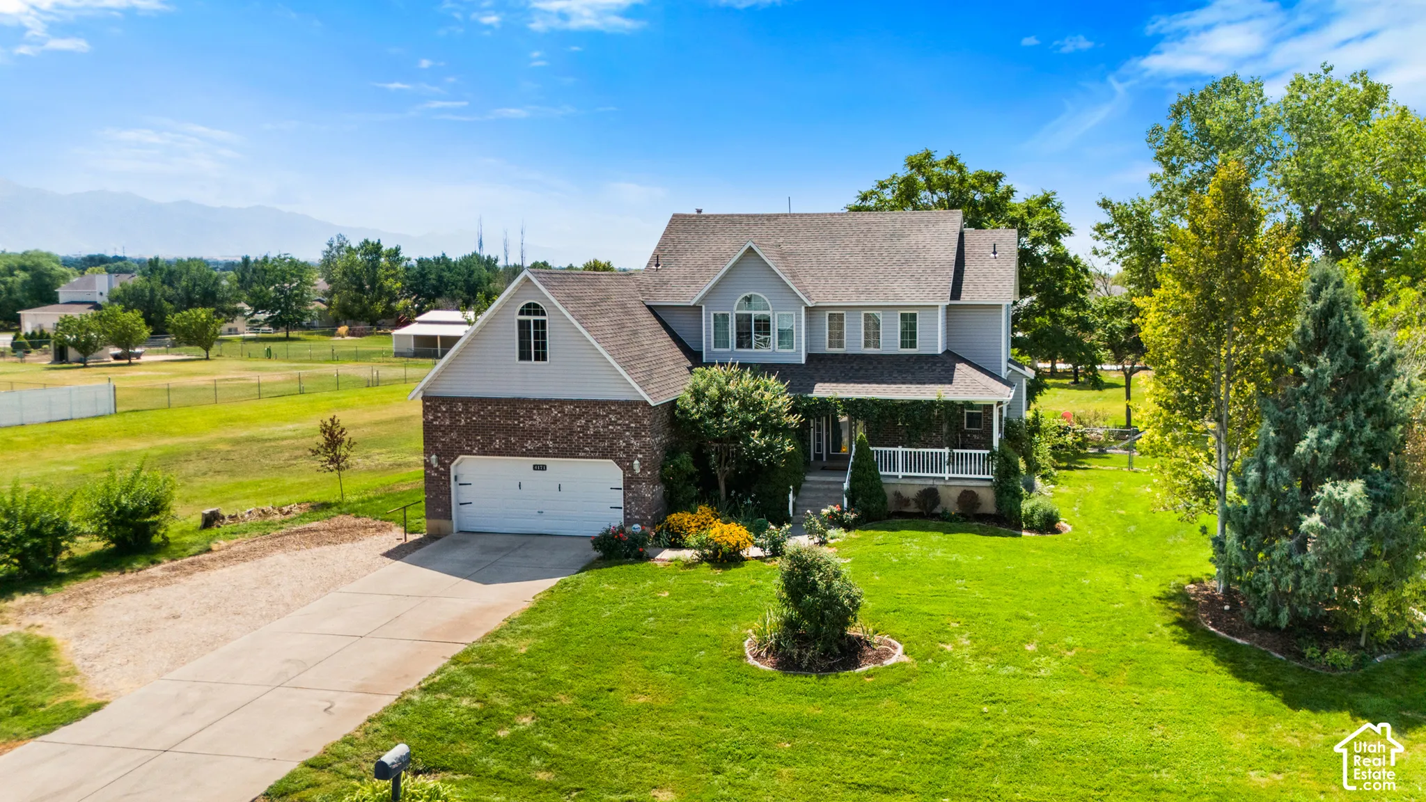 Two-story property featuring a brick and siding exterior, an attached two-car garage, a covered front porch, and mature landscaping