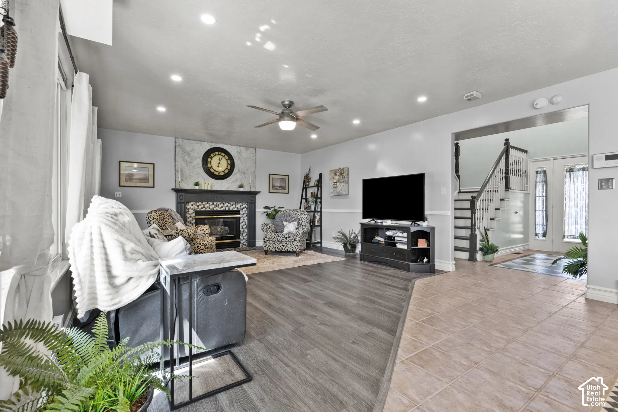 Recessed lighting, ceiling fan, fireplace with a tiled surround and mantel, wood-finish flooring, and a staircase with white risers and dark treads