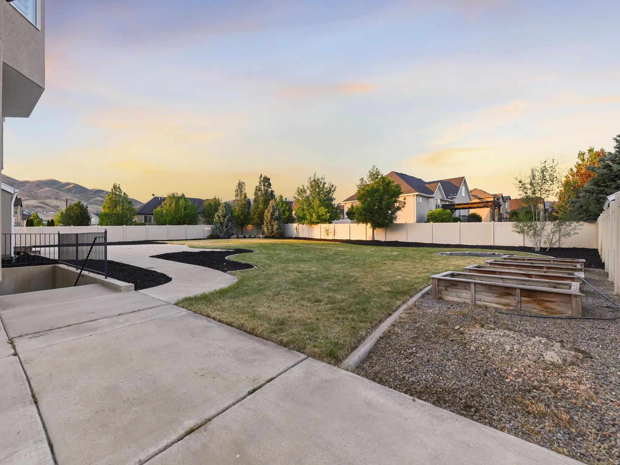 Expansive backyard featuring a large lawn area, mature trees, and multiple raised garden beds