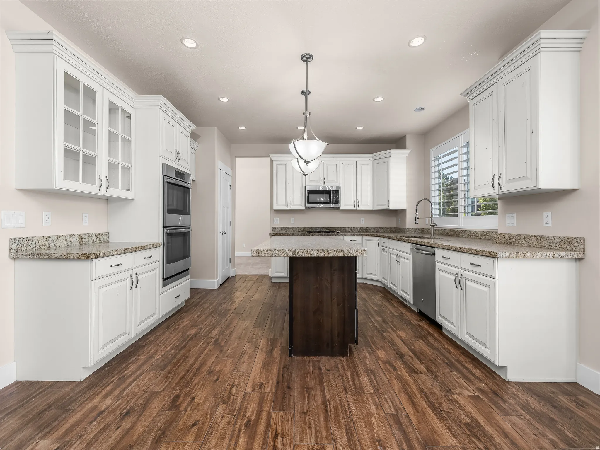 Kitchen featuring white cabinetry, wood-finish flooring, granite countertops, a center island with a dark wood-finish base, and stainless steel appliances