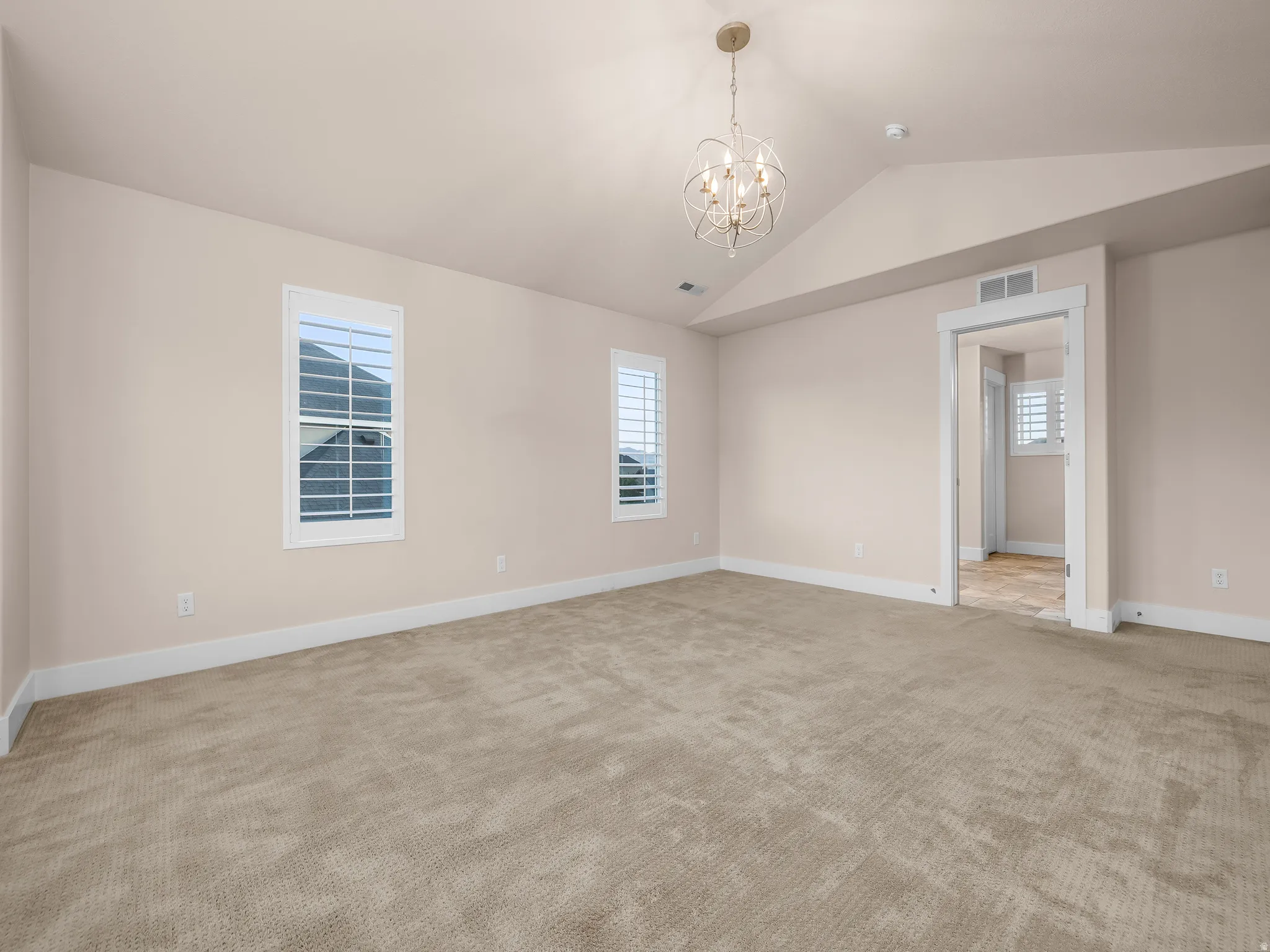 Vaulted ceiling with an orb chandelier, textured carpet, white window shutters, and white trim