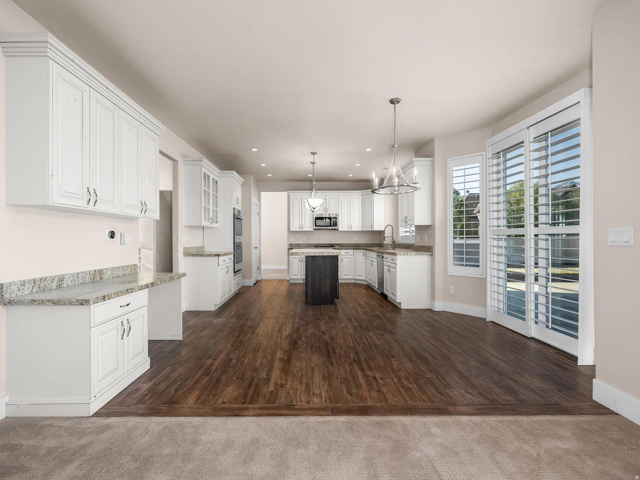 White cabinetry with granite-style countertops, wood-finish flooring, recessed lighting, and sliding glass doors with interior shutters