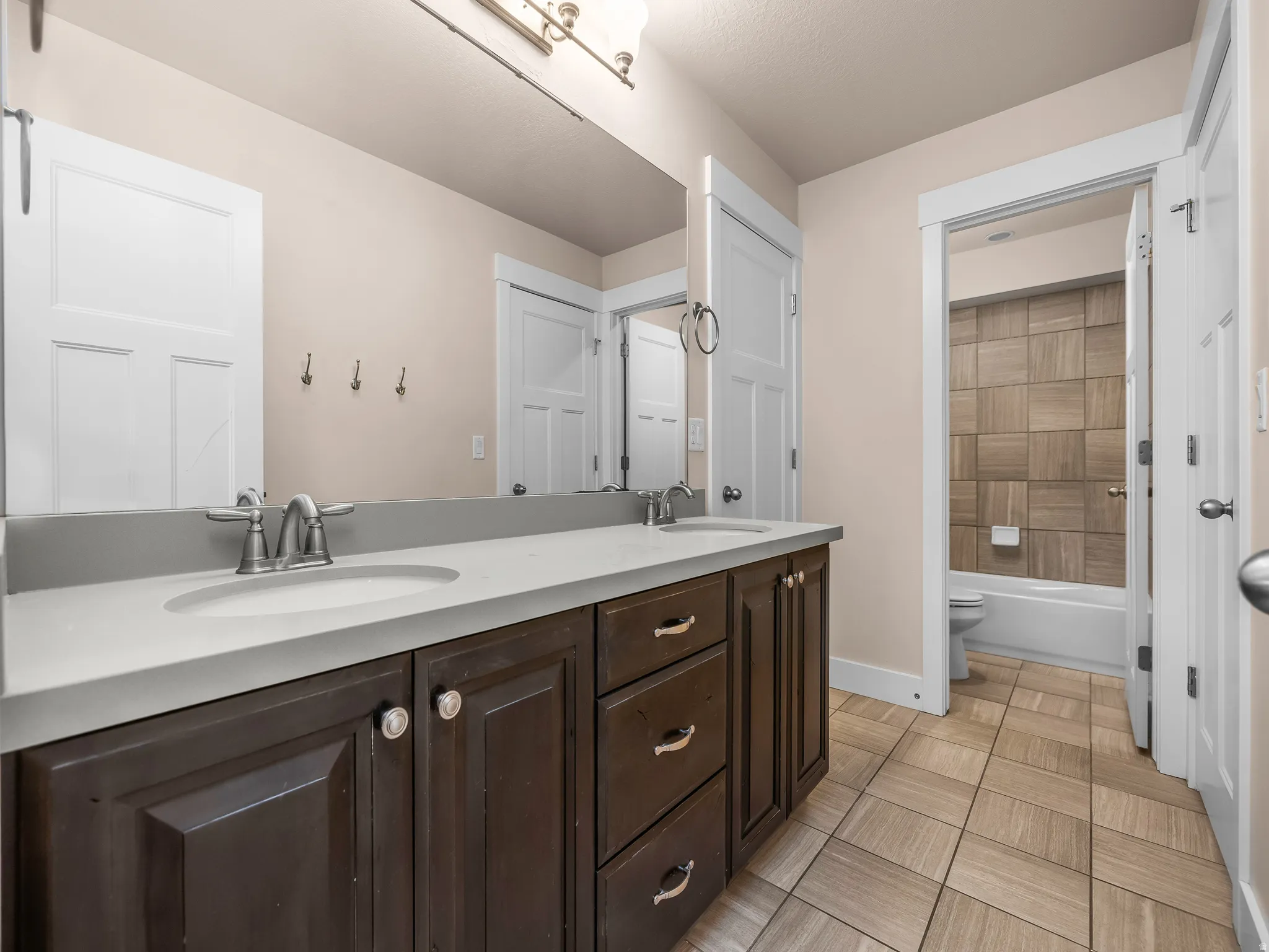 Dual sink vanity with dark wood-finish cabinetry, light-toned countertop, and brushed nickel fixtures