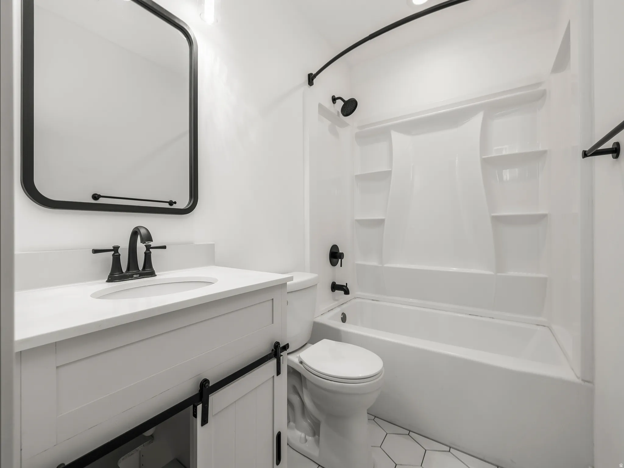 Bathroom featuring a white vanity with barn door style cabinetry, matte black fixtures, a white bathtub with integrated shelving, and hexagonal floor tiling