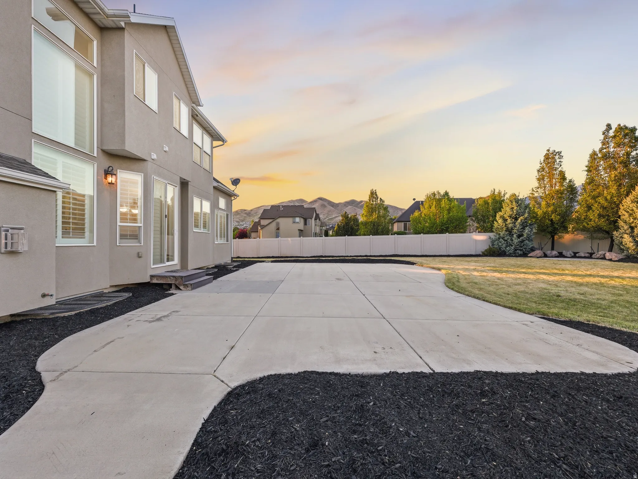 Concrete patio with dark mulch landscaping and a manicured lawn