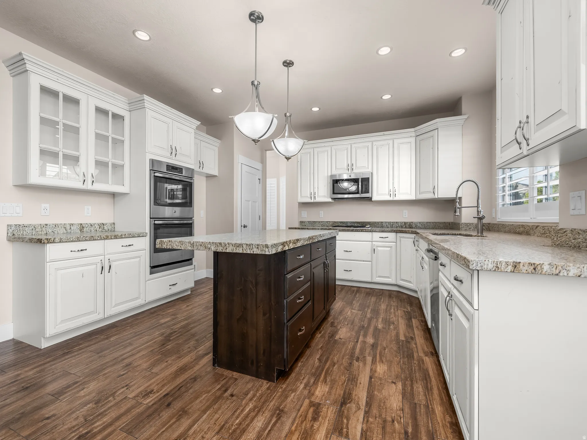 Well-appointed kitchen featuring white cabinetry, a central island with wood-finish cabinetry, light-toned countertops, and stainless steel appliances