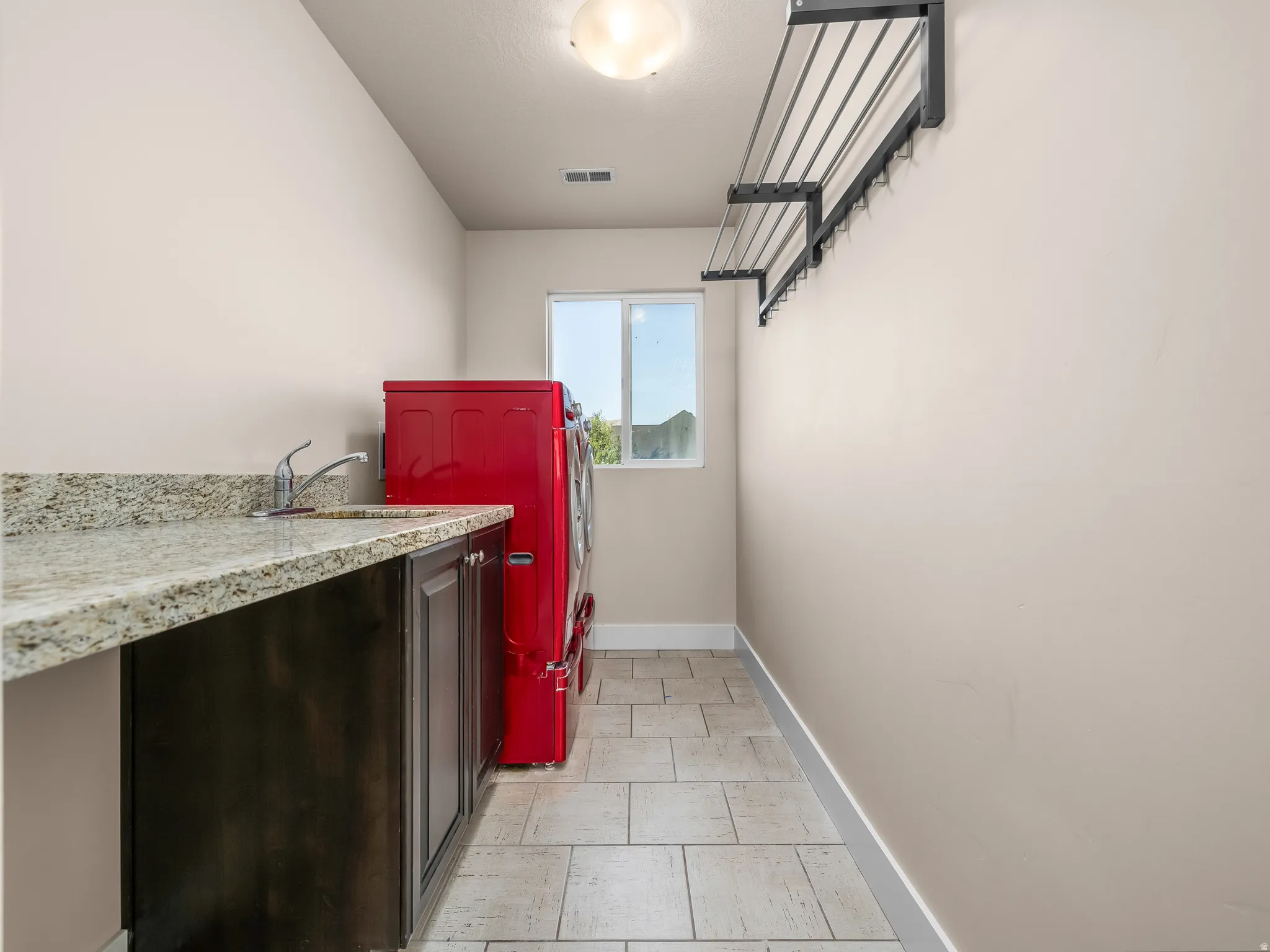 Built-in cabinetry with a stone-finish countertop, single basin sink, tiled flooring, and a wall-mounted drying rack