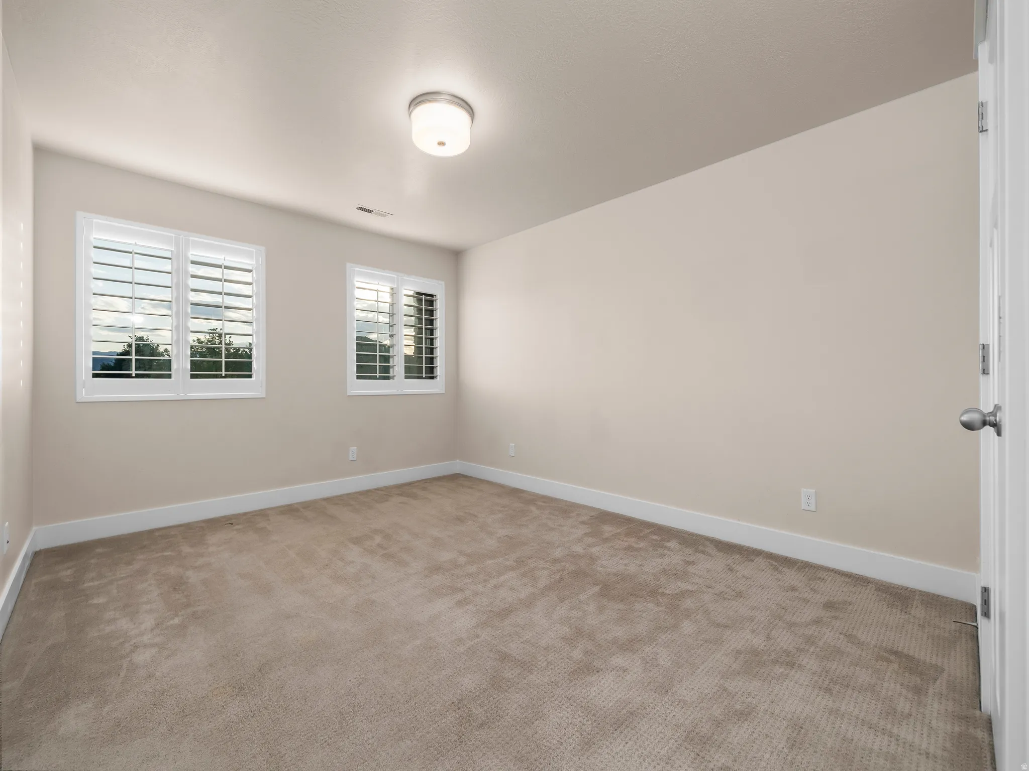 Neutral-toned carpet flooring, two windows with white plantation shutters, white baseboards, and a semi-flush mount ceiling fixture