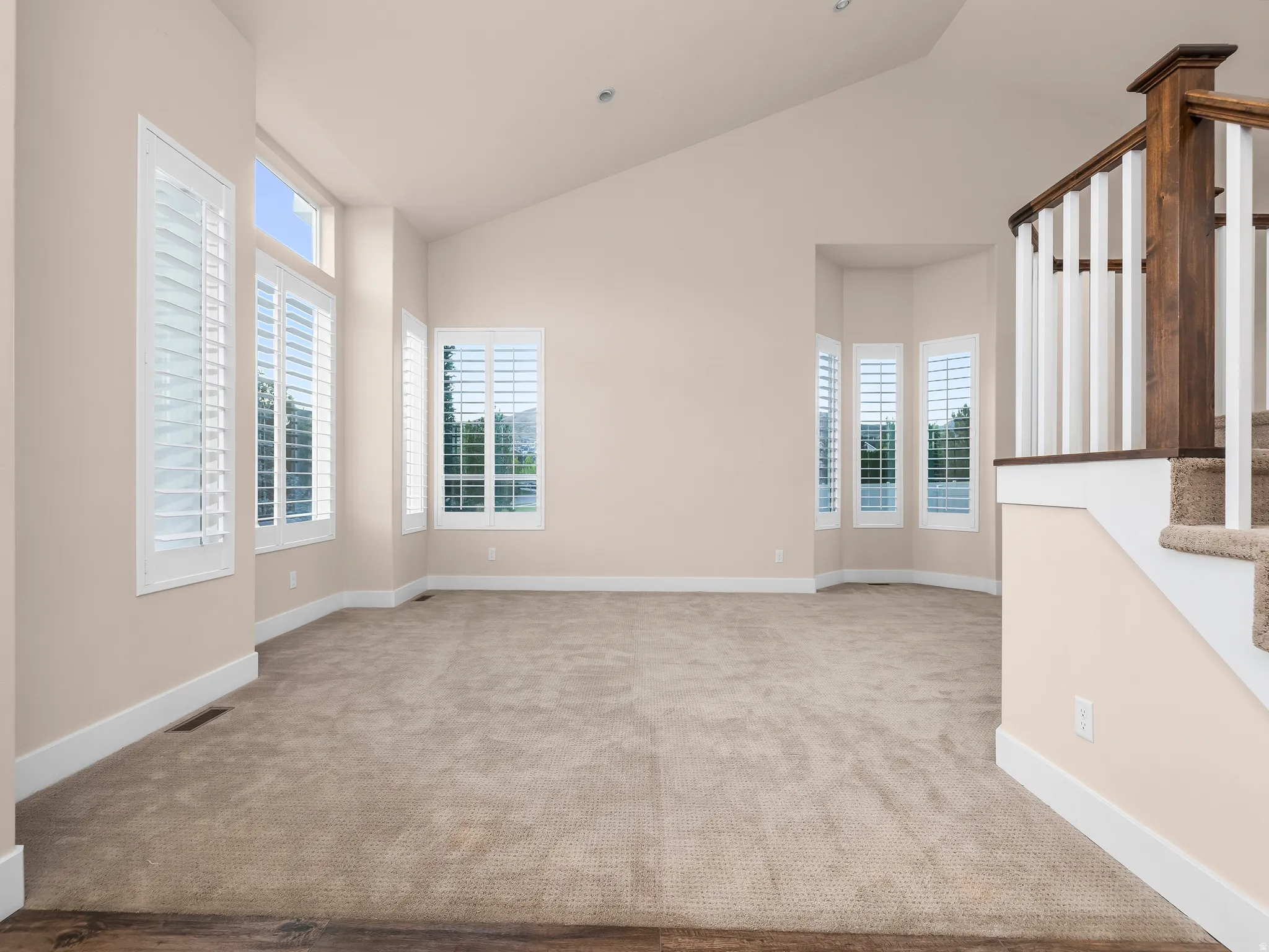 Vaulted ceilings with recessed lighting, multiple windows with white plantation shutters, neutral carpet, and a wood and white banister